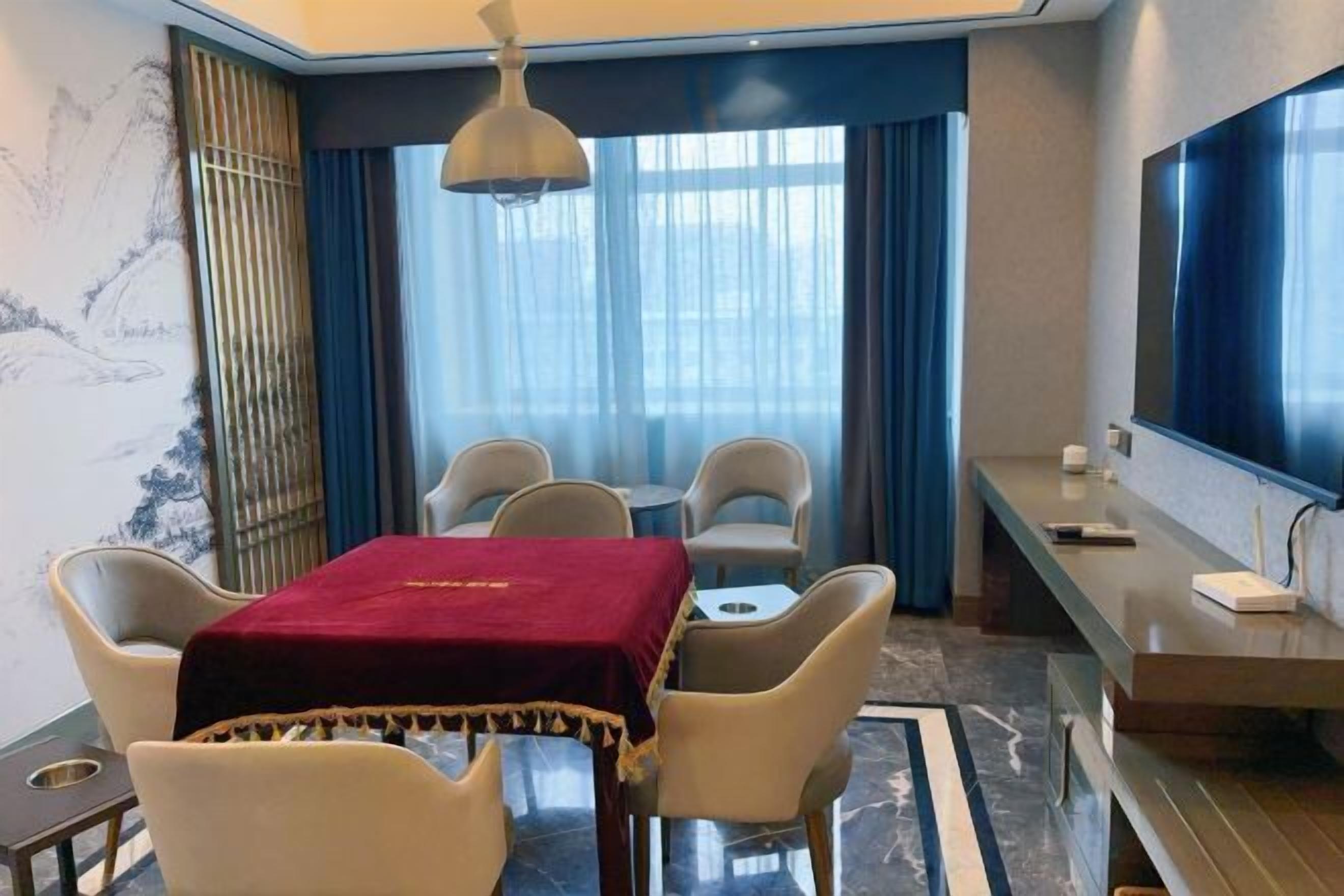 Habitación de hotel con comedor, televisión y un amplio ventanal con cortinas.