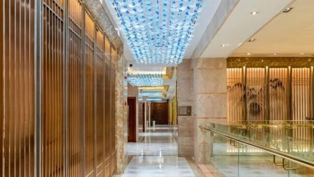 A modern hotel corridor with a reflective floor, vertical wooden panels on one side, and a glass railing on the other. - Yangzi International Hotel (Liyang)