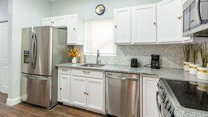 Une cuisine moderne avec des armoires blanches, des appareils en acier inoxydable, un comptoir en granit et une horloge au mur.