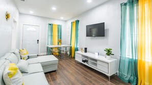 Un salon moderne avec un canapé d’angle, un meuble de rangement blanc et un téléviseur à écran plat fixé au mur.