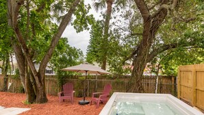 Un bain à remous entouré d’arbres, avec deux fauteuils Adirondack et un parasol de patio.