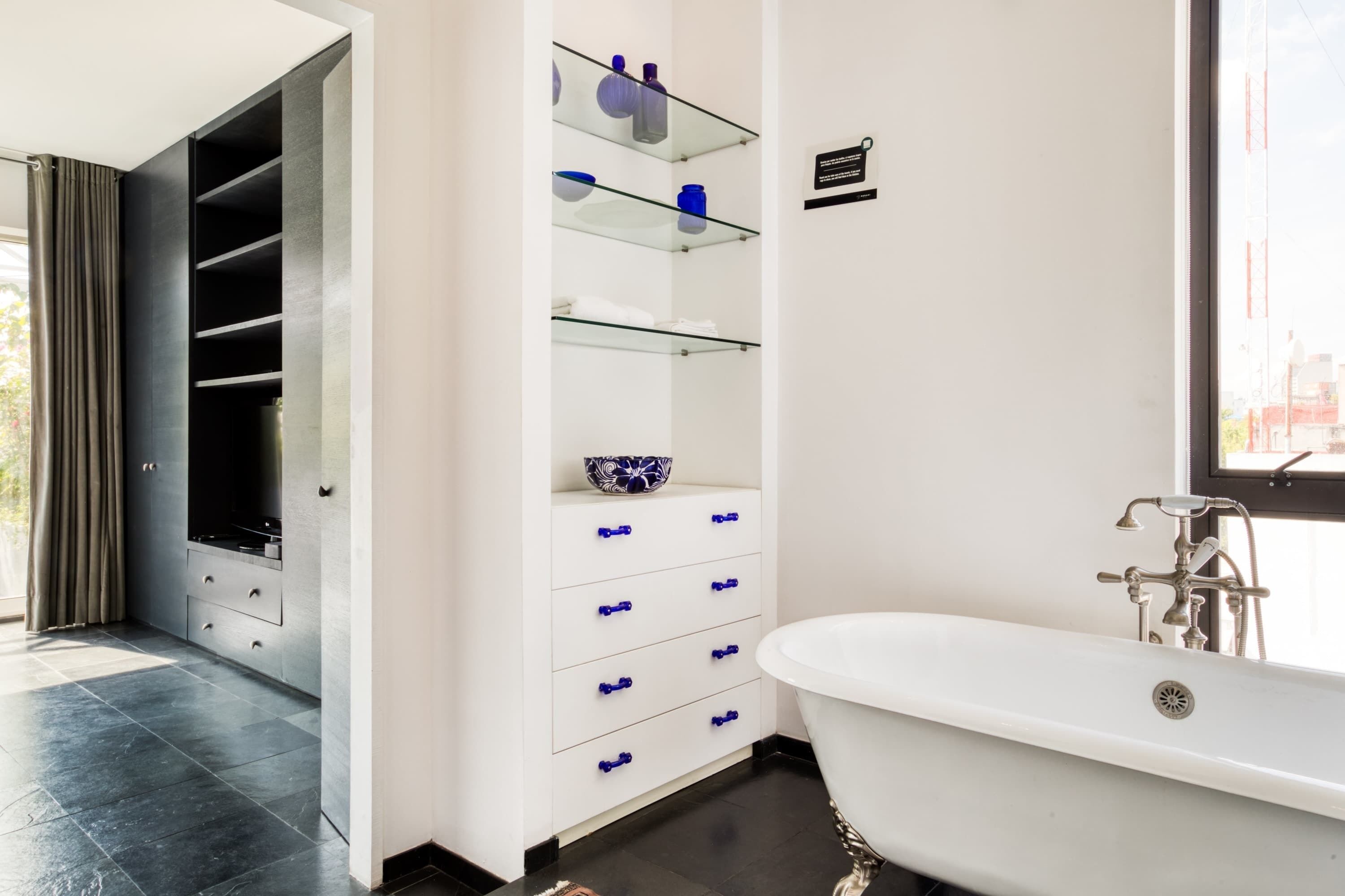 Une salle de bain moderne avec une baignoire sur pieds, des étagères en verre où sont rangés les articles de toilette et un placard intégré.