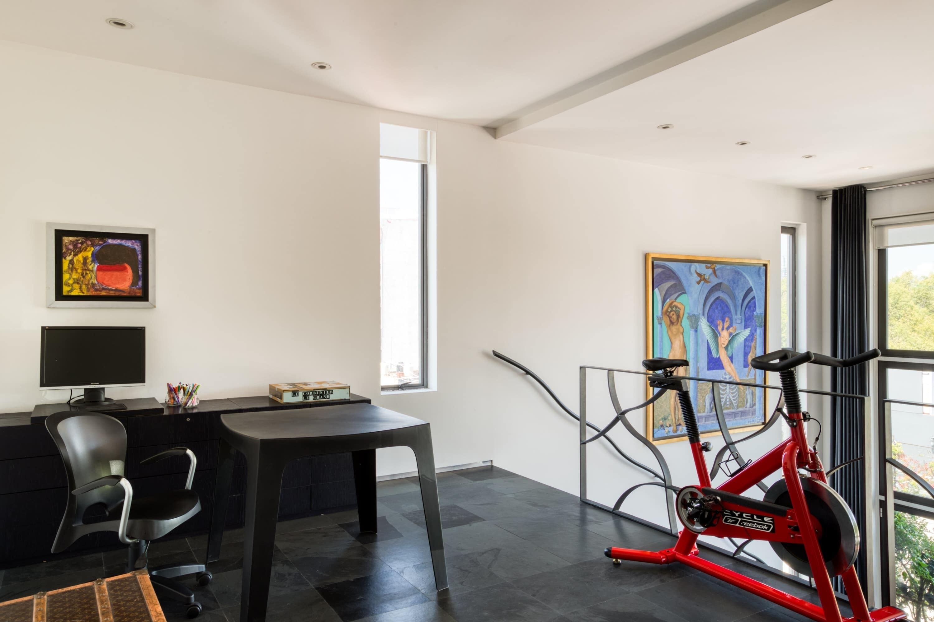 Un espacio de oficina moderno con un escritorio, una silla y una bicicleta estática roja.