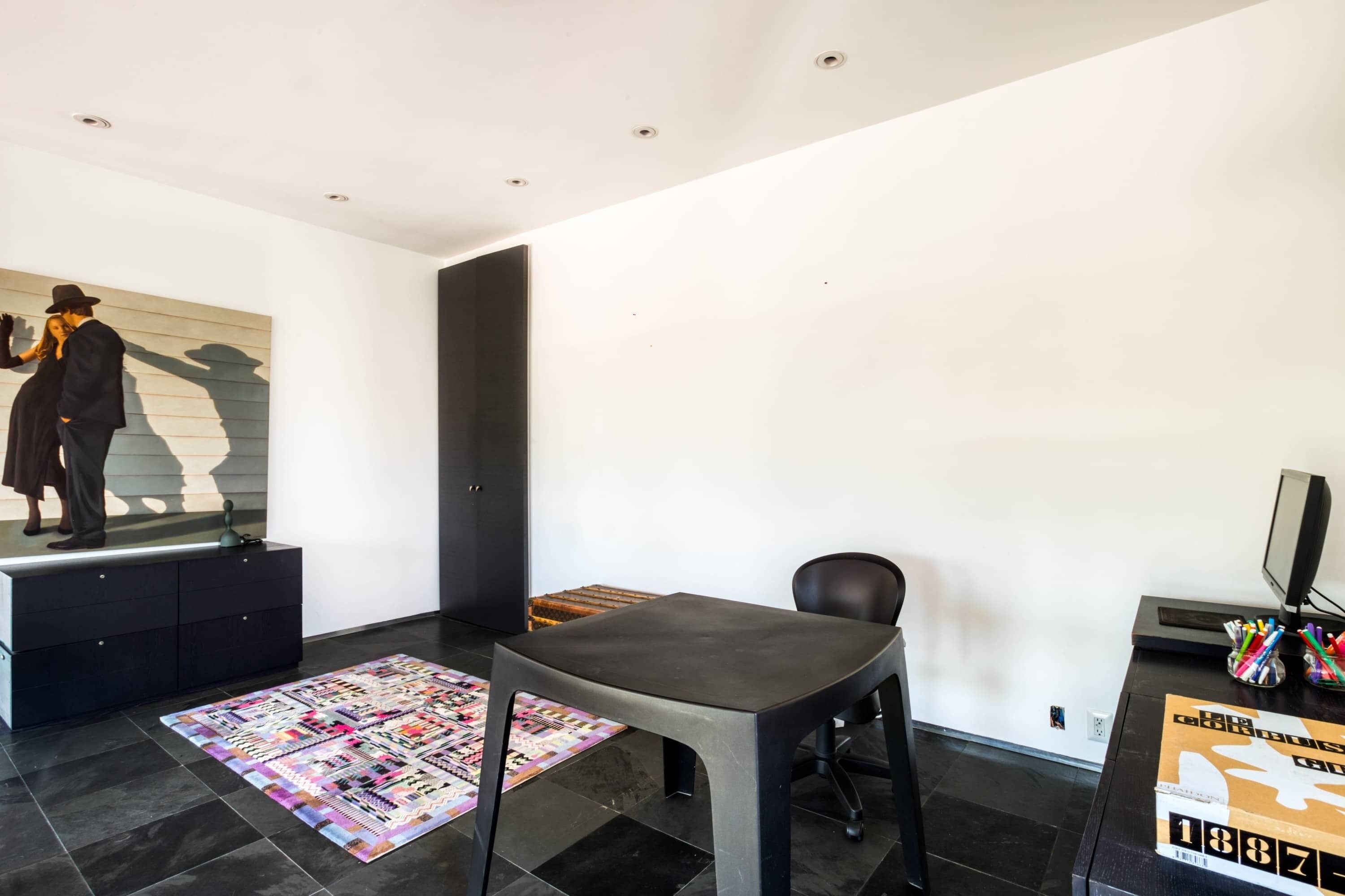 Une pièce moderne avec un bureau noir, une chaise, un tapis coloré, un meuble noir et un mur sur lequel on aperçoit l’ombre d’une personne.