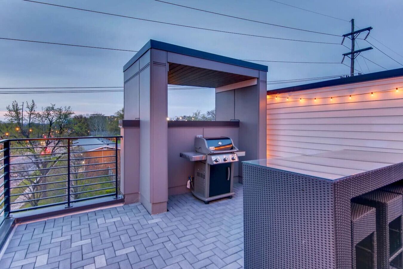 An outdoor patio with a grill, a covered seating area, and a string of lights.
