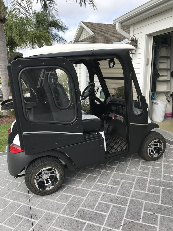 A compact, black and white golf cart parked in front of a house with a garage. - Beautiful Ranch close to Sumter Landing and Cane Gardens Country Club (The Villages)