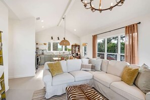 A spacious living area with a white sectional sofa, a zebra-patterned ottoman, and a large window with curtains.