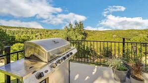 Ein Grill aus Edelstahl auf einer Terrasse mit Blick auf eine grüne Landschaft und einen klaren Himmel.