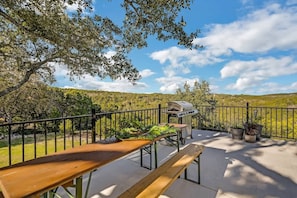 Eine Terrasse im Freien mit Grill, einem Holztisch und Blumentöpfen.