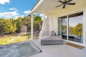 A covered outdoor area with a hot tub, a cushioned seating area, and a pergola with a canopy.