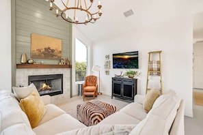 A living room with a fireplace, a sofa set, a chandelier, and a television.