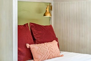 A bed with two red pillows and a peach-colored pillow, a gold lamp, and a green wall.