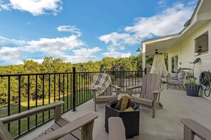 A balcony with outdoor seating, a fire pit, and a view of a green landscape.