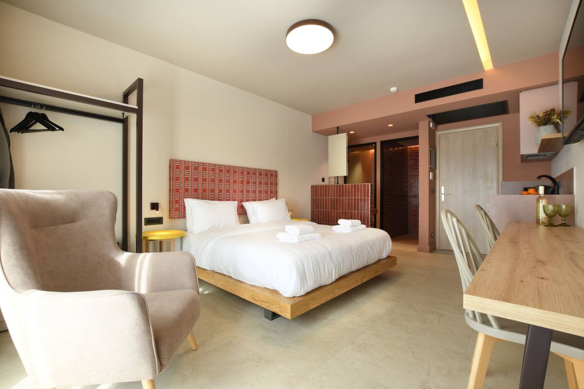 Une chambre d’hôtel moderne dotée d’un grand lit, d’un coin salon avec un fauteuil, d’une table à manger et d’une petite table d’appoint.