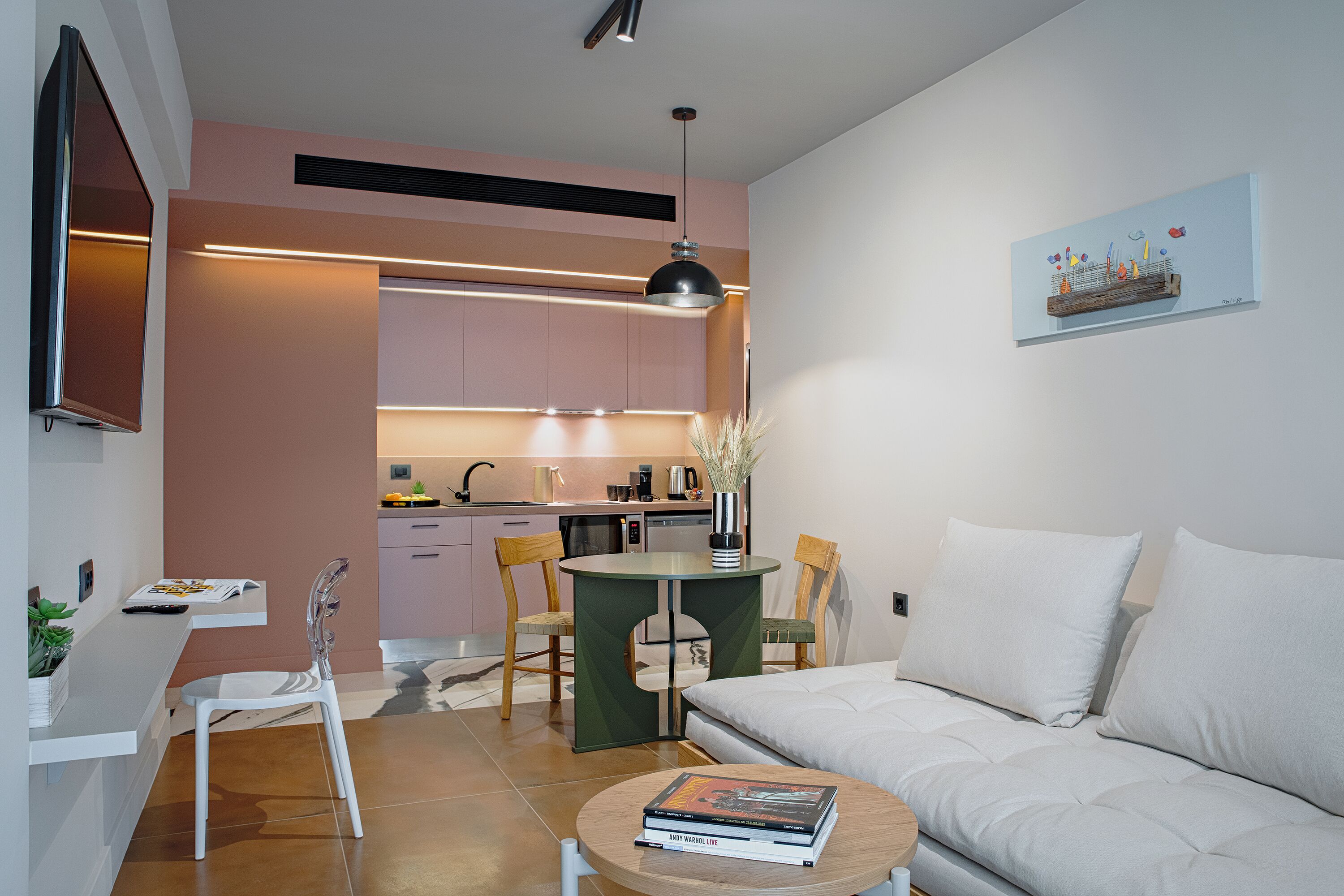 A modern living room with a sofa, a coffee table with books, a dining area with chairs, and a kitchen in the background.