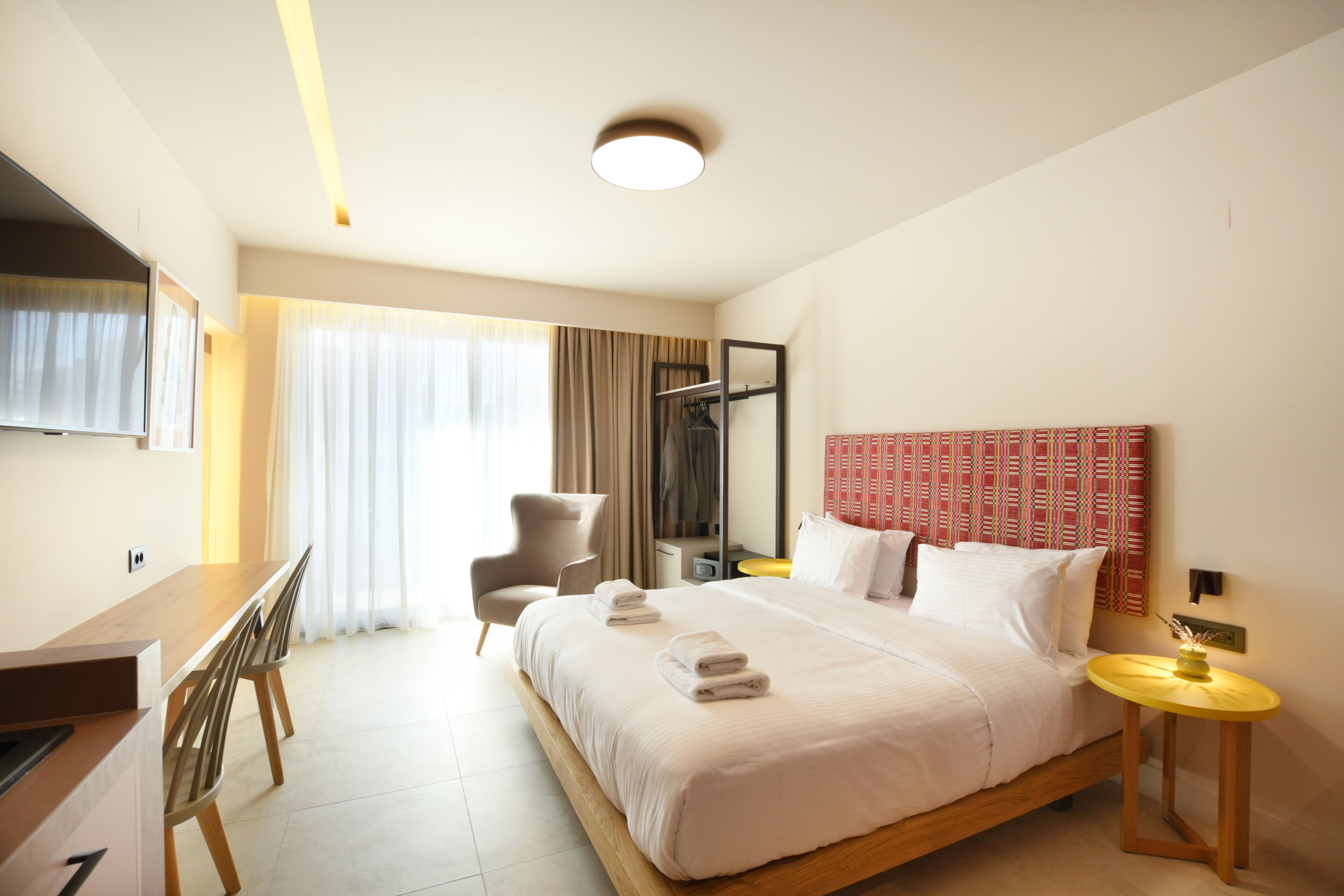 Una habitación de hotel con cama, escritorio, silla, mesita de noche y espejo.