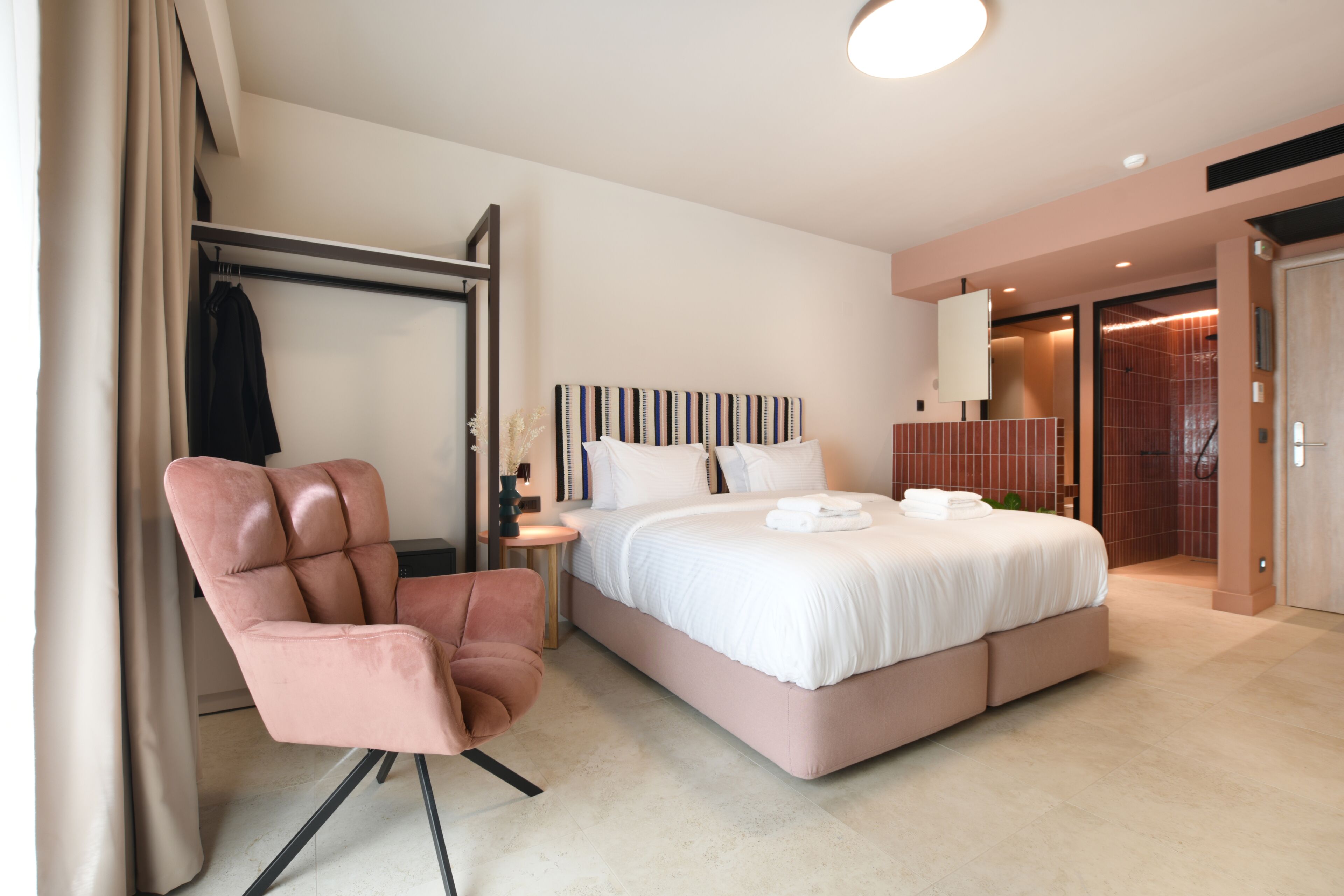 A modern hotel room with a large bed, a seating area with a chair, and a wardrobe.