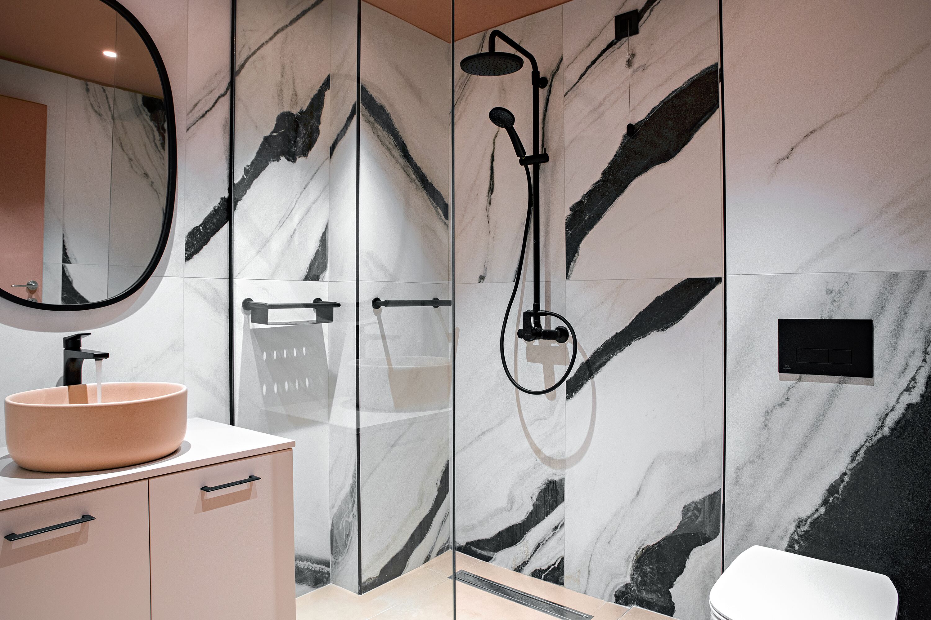 A modern bathroom with a large mirror, a beige sink, a glass-enclosed shower, and marble walls.