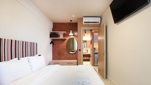Une chambre d’hôtel comprenant un lit, un téléviseur à écran plat fixé au mur, un petit bureau avec une chaise, un miroir et une porte donnant accès à la salle de bain.