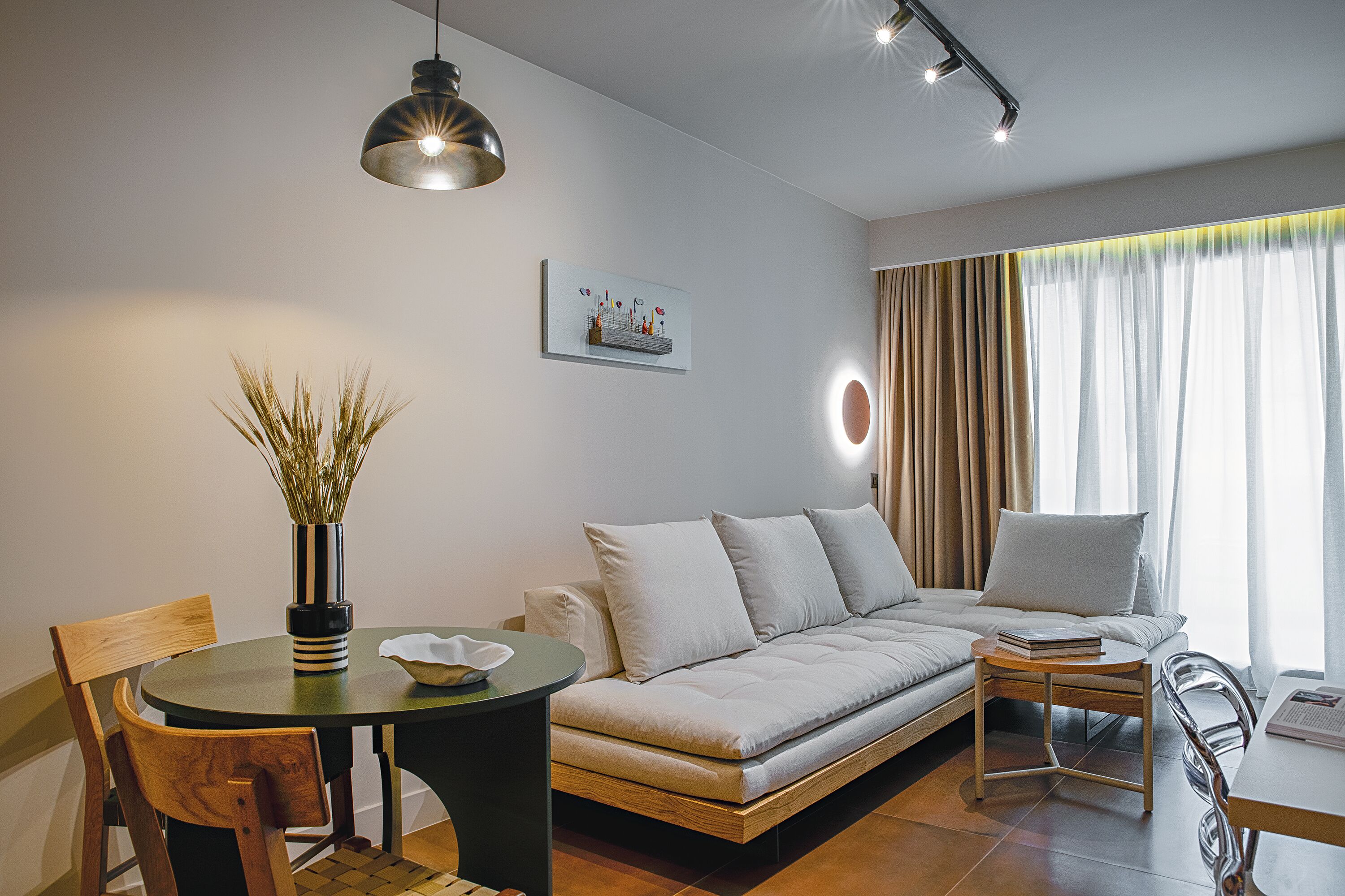 A modern living room with a sofa, a dining table, and chairs. There is a vase with plants on the table.
