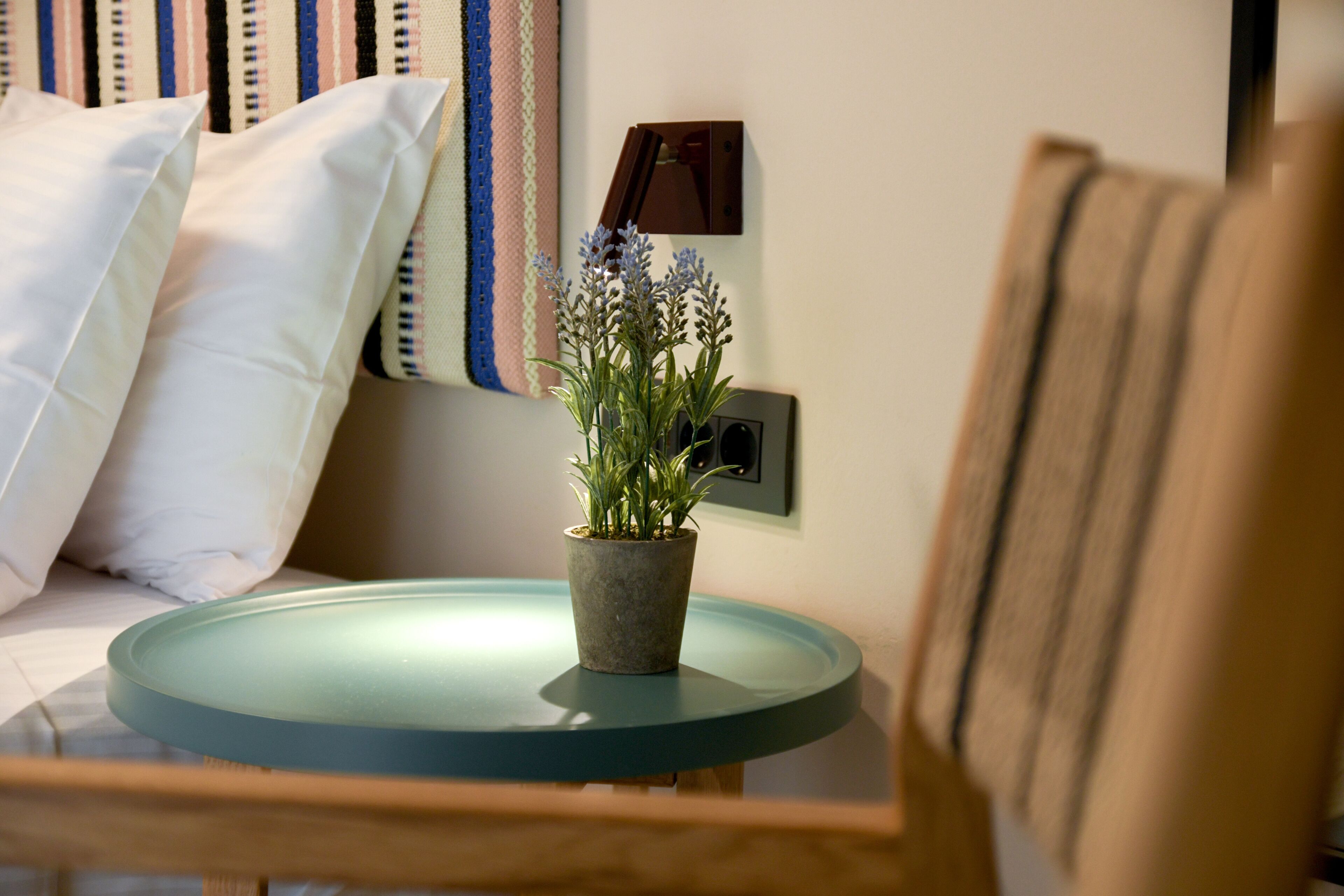 A small round table with a potted plant, a white pillow, and a wall-mounted light switch.