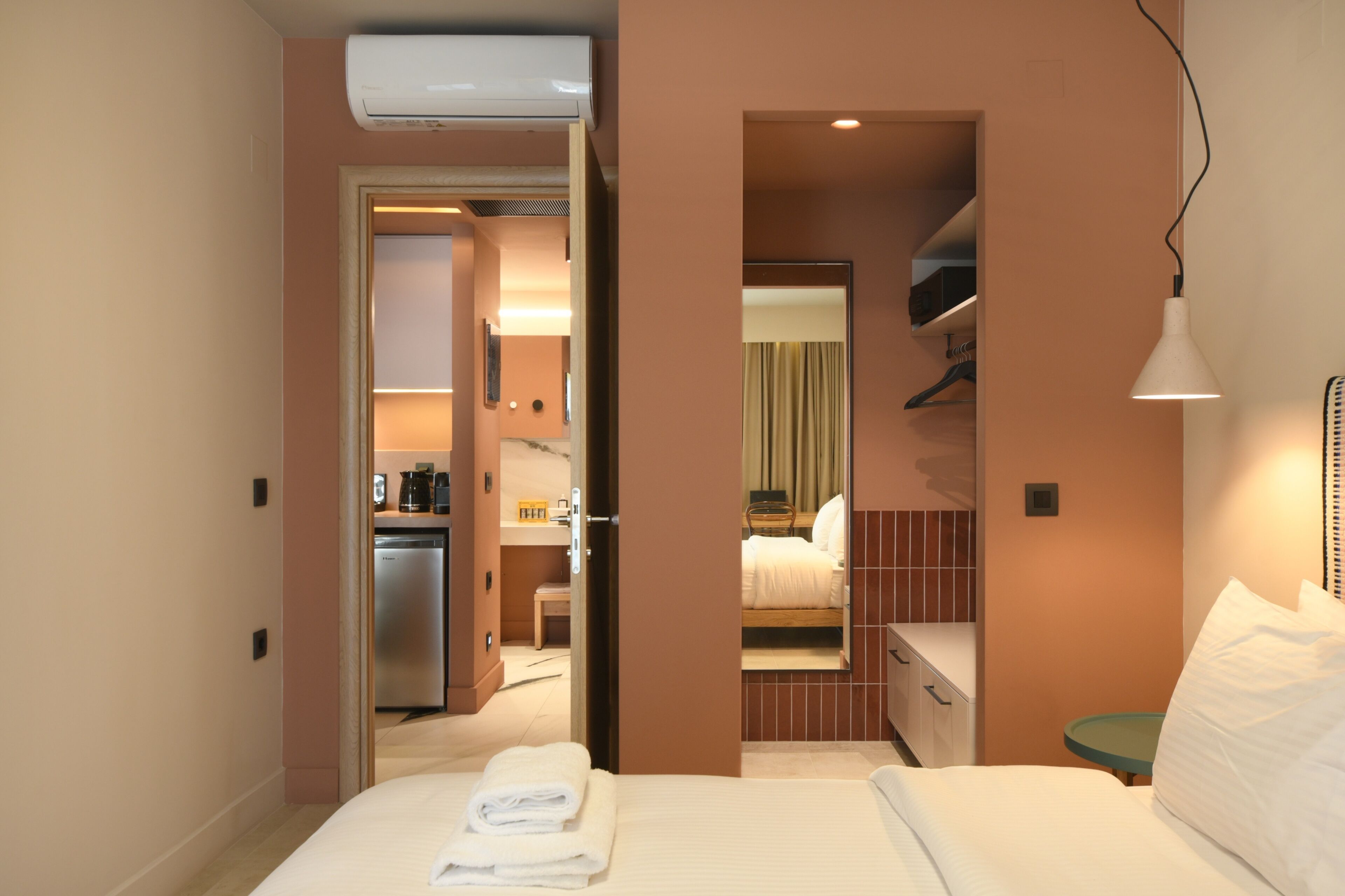 A hotel room with a bed, a desk, a chair, a mirror, and a hanging light fixture.