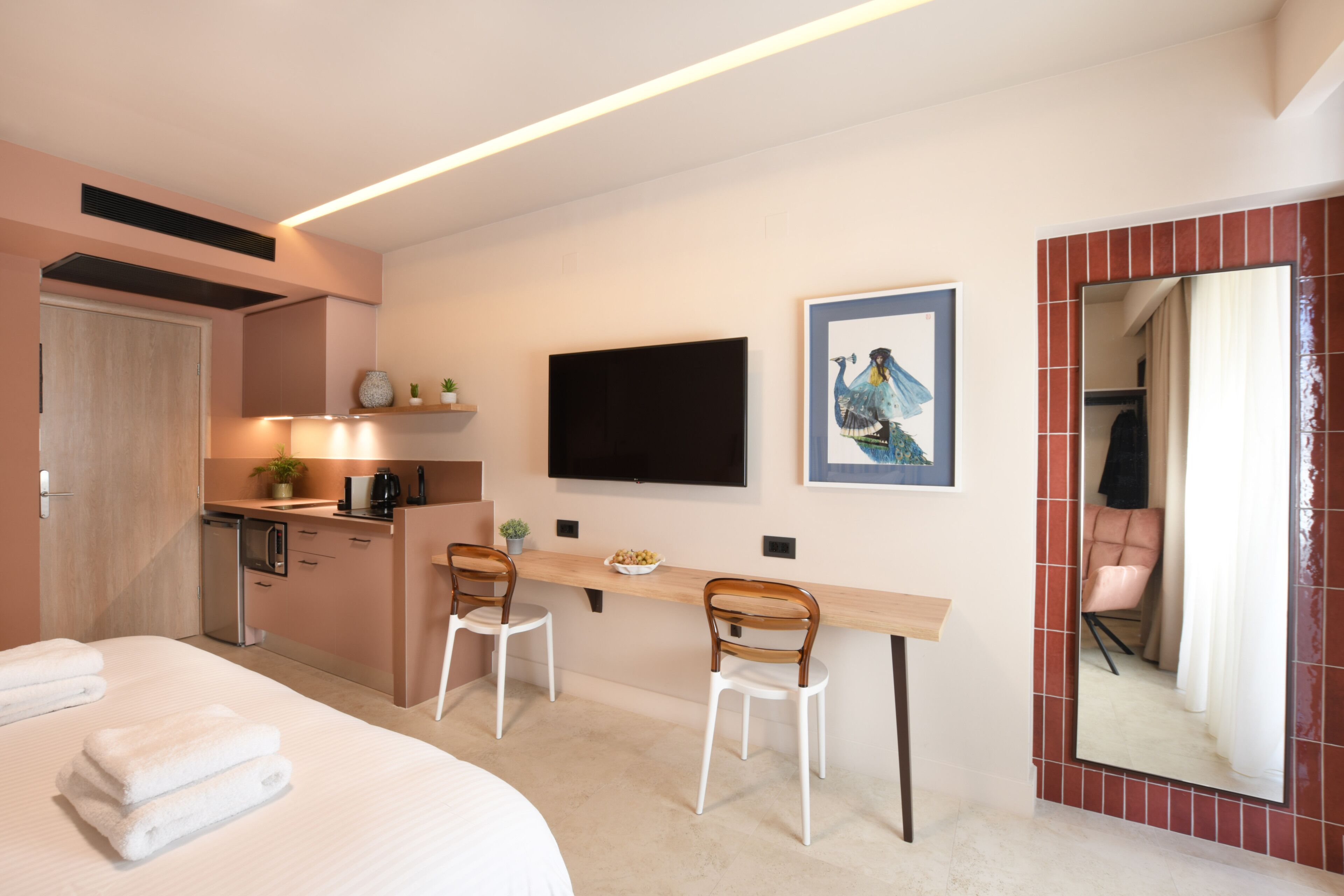 Una habitación de hotel con una cama, dos sillas, un escritorio, un televisor y un espejo.