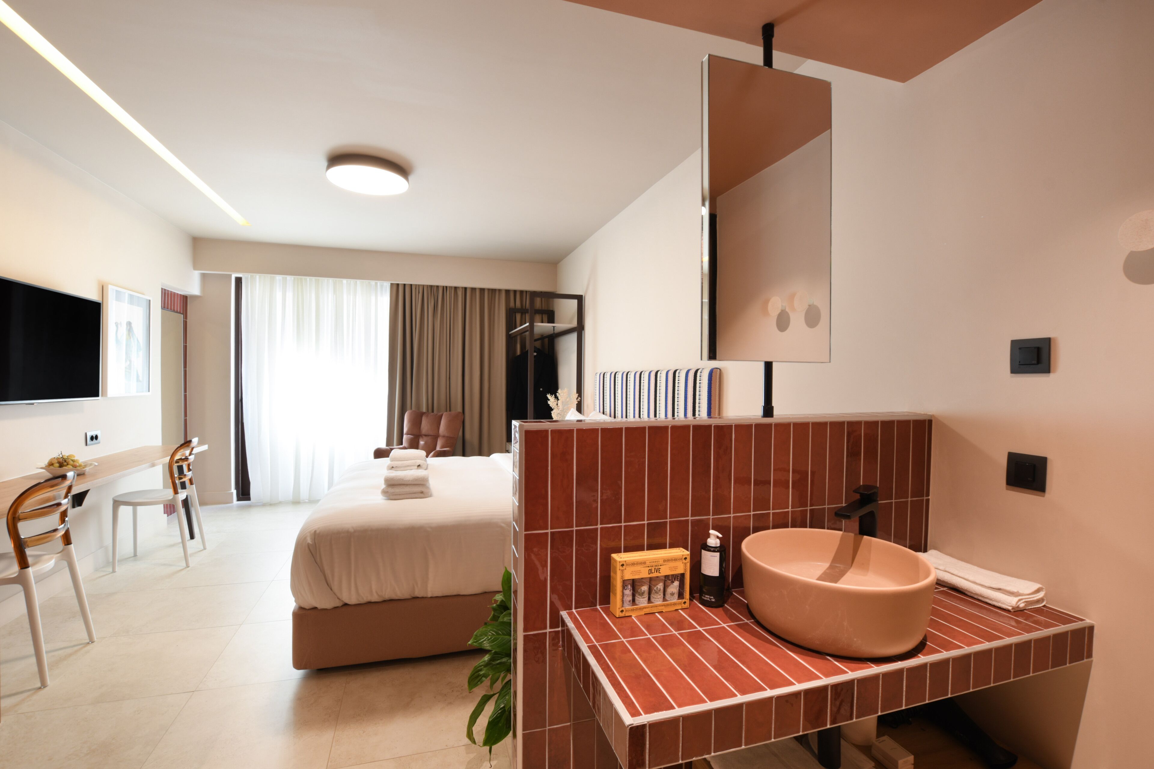 A modern hotel room with a large bed, a desk, and a bathroom with a large sink and mirror.