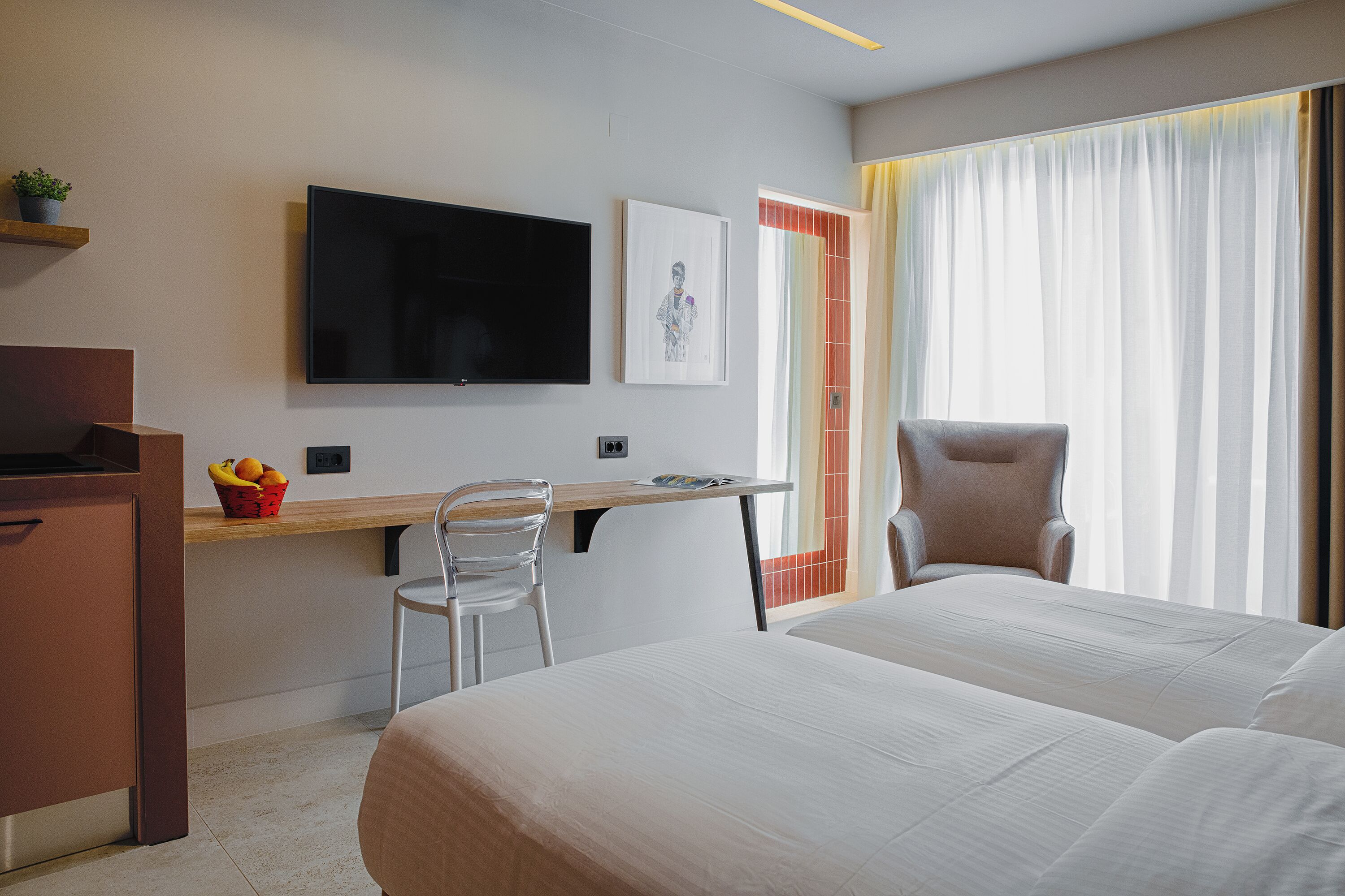 A hotel room with a bed, a desk with a chair, a television, and a window with curtains.