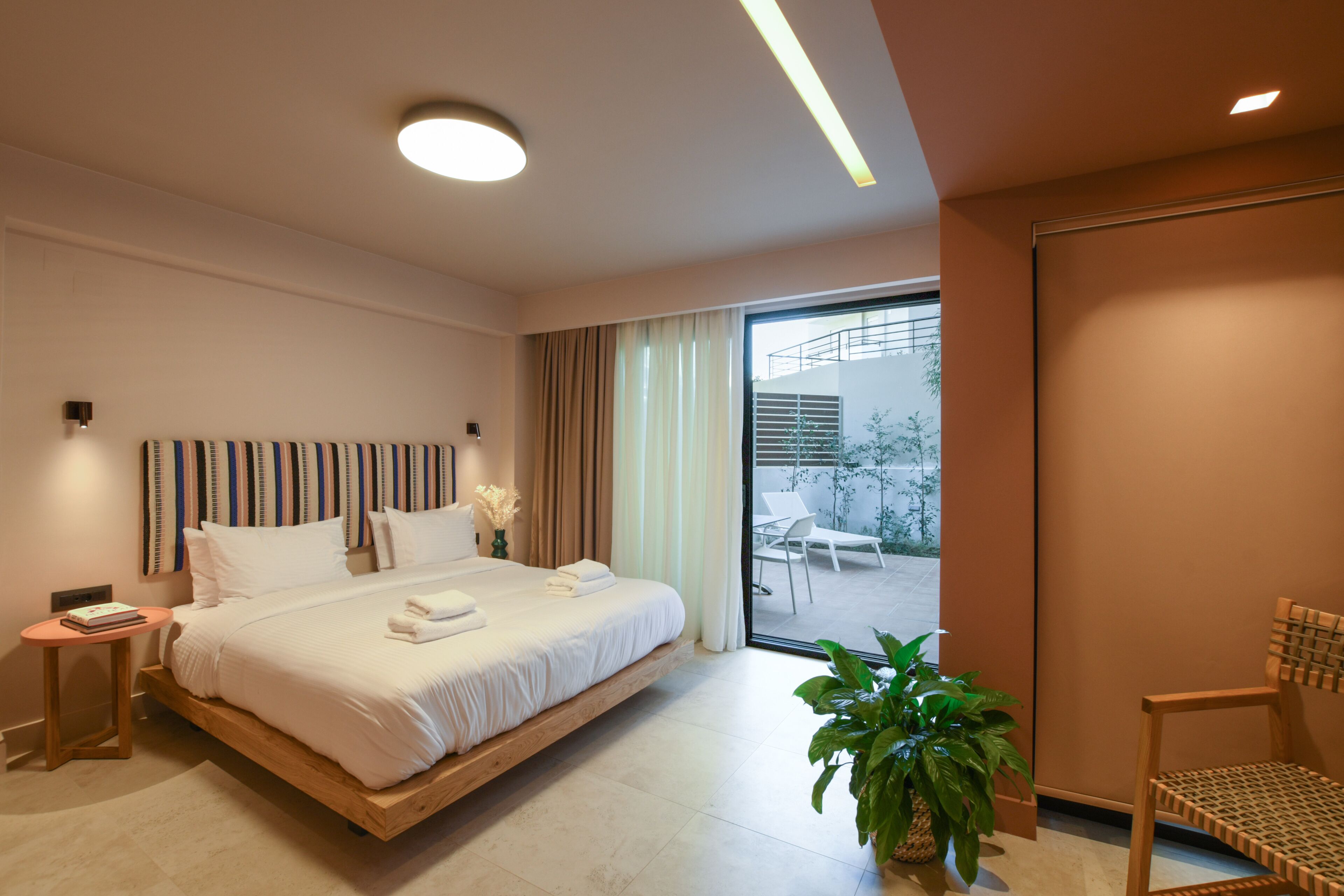 Habitación de hotel moderna con una cama grande, una mesita auxiliar, una planta en maceta y vistas al exterior.