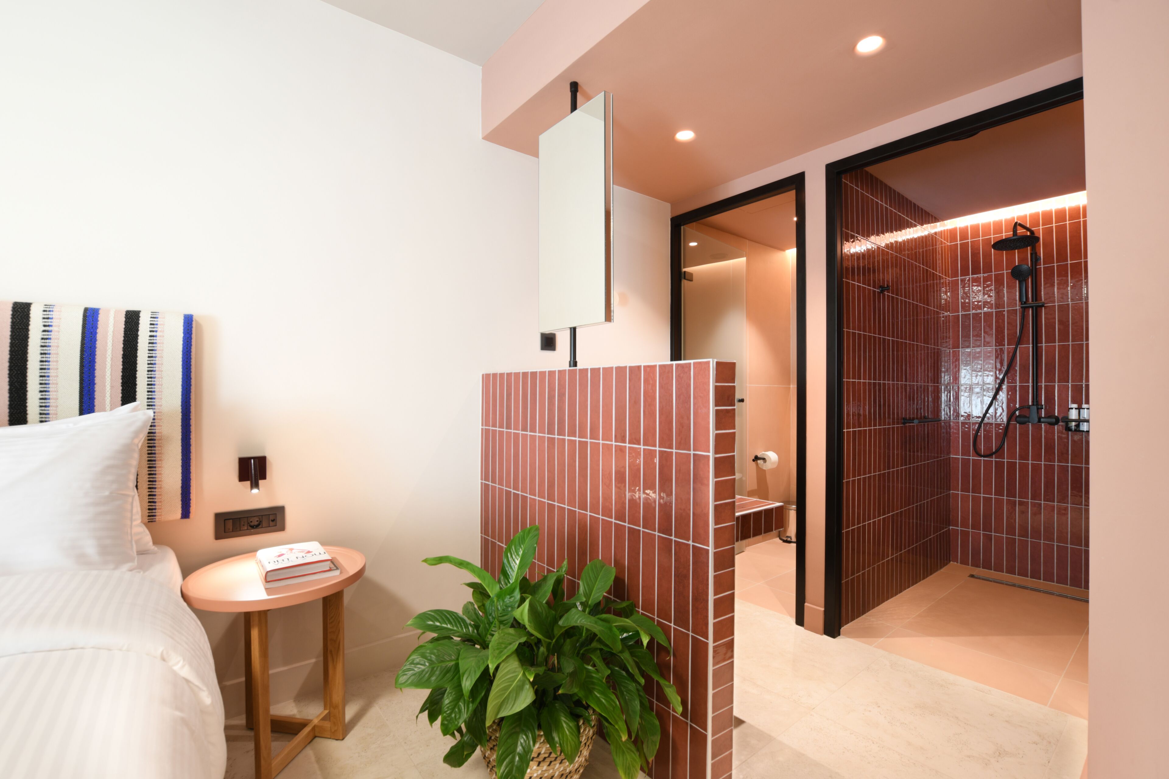 A modern hotel room with a bed, bedside table, and a potted plant.