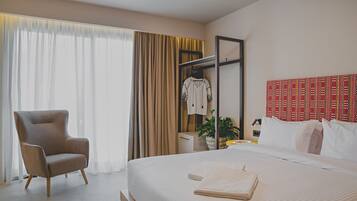Een hotelkamer met een groot bed, een zithoek met een fauteuil, een kledingkast en een hoofdeinde met een rood patroon.