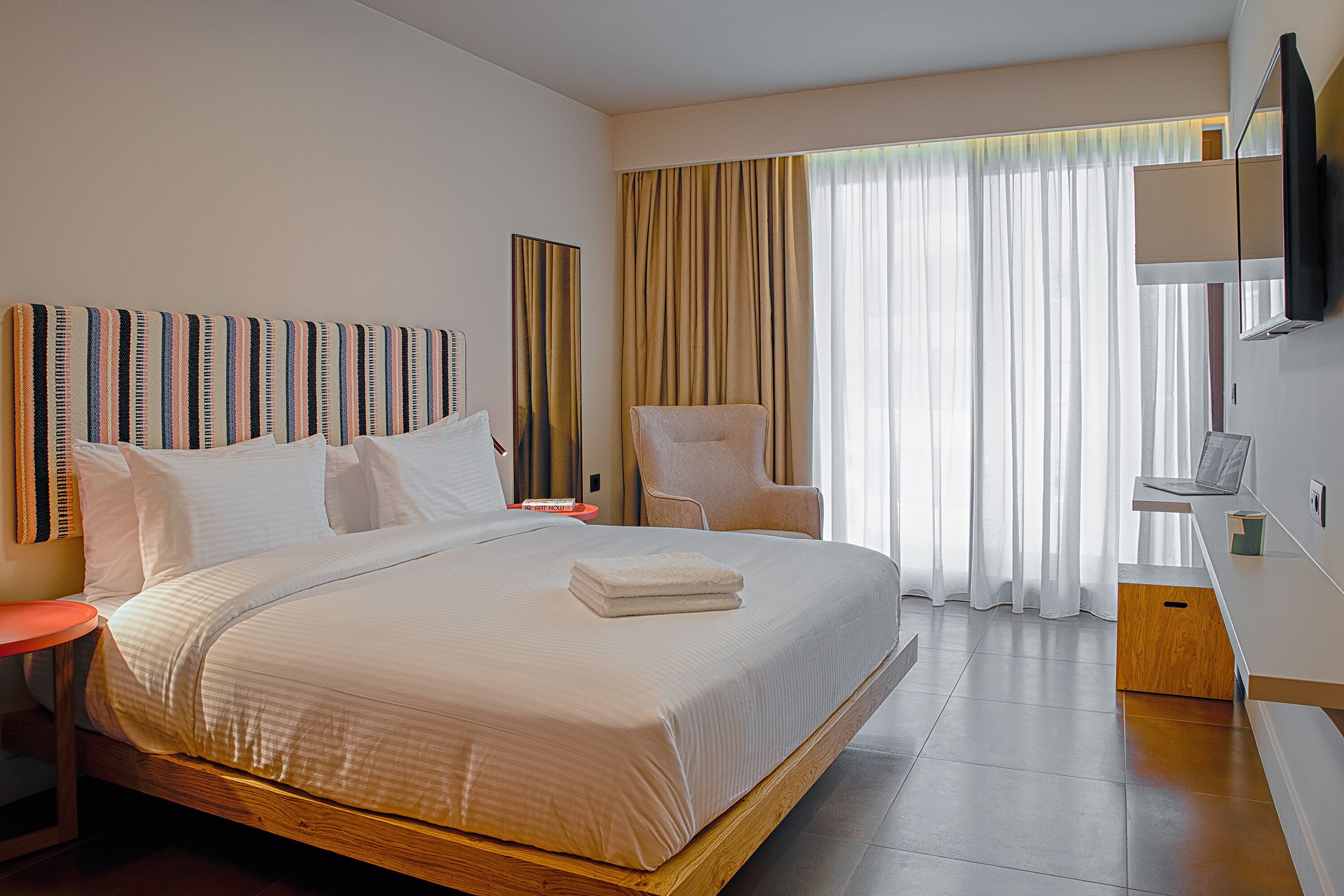 A modern hotel room with a large bed, a chair, a desk, and a TV.