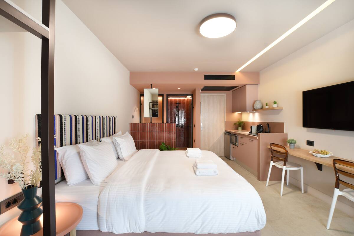 Une chambre d’hôtel moderne équipée d’un grand lit, d’un bureau, d’une chaise, d’une télévision et d’une kitchenette.