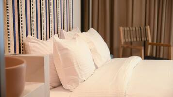 Ein ordentlich bezogenes Bett mit weißen Leinentüchern, ein Holzstuhl und gestreifte Vorhänge in einem Hotelzimmer.