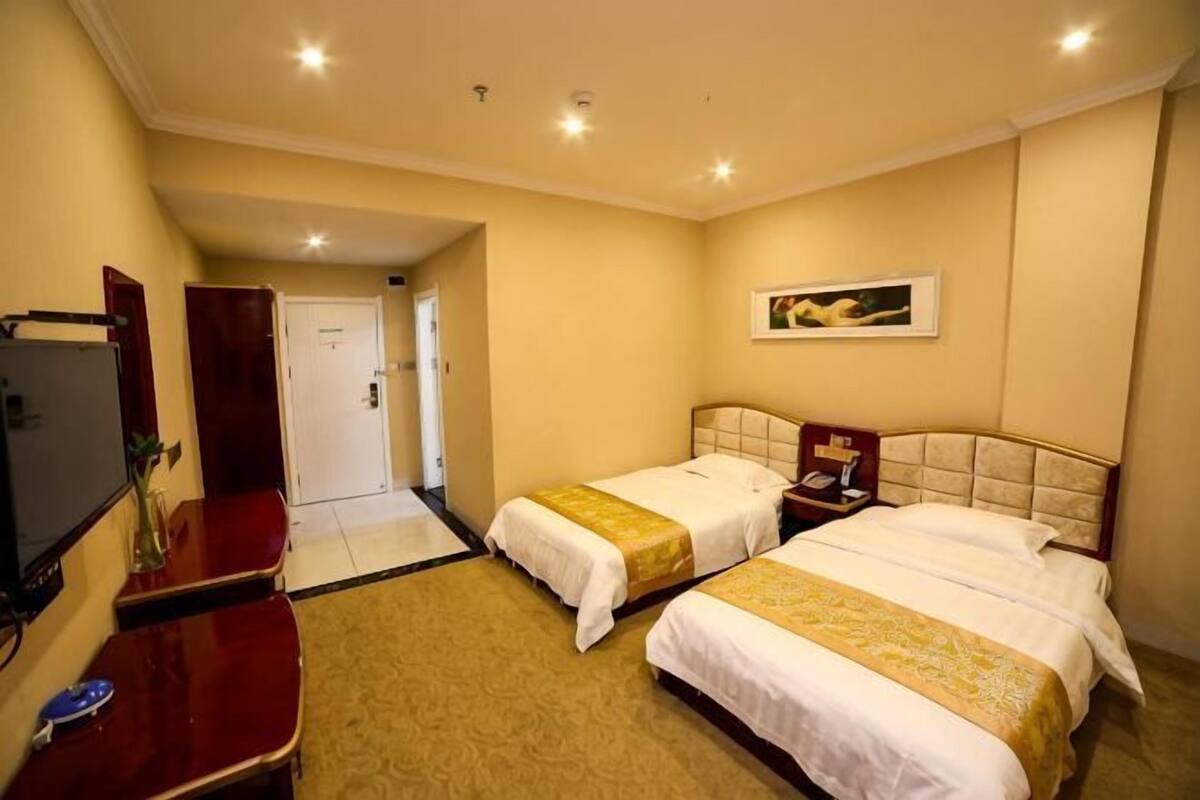 Une chambre d’hôtel avec deux lits, un bureau, une télévision et une porte donnant sur une autre chambre.