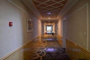 Un couloir d’hôtel avec un tapis à motifs, une main courante et un plafond orné d’un motif en réseau.