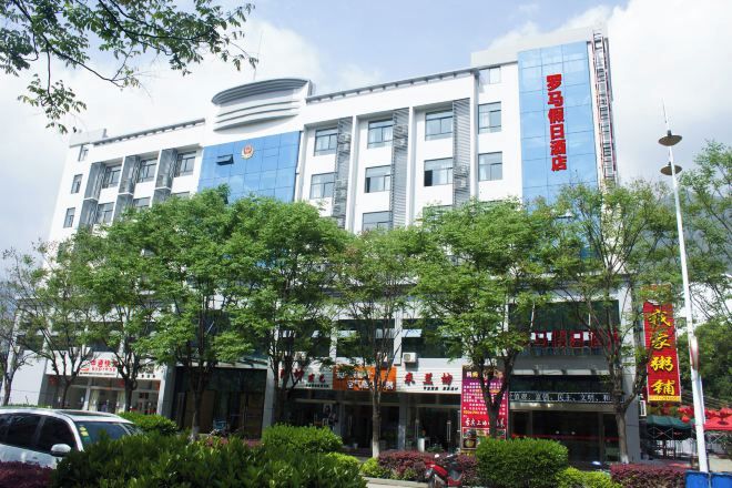 A multi-story building with a blue and white facade, surrounded by trees and a street with parked cars.