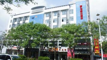A multi-story building with a blue and white facade, surrounded by trees and a street with parked cars.