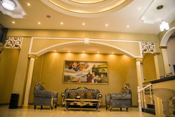 A lobby with a grand staircase, a large painting, and two ornate sofas.