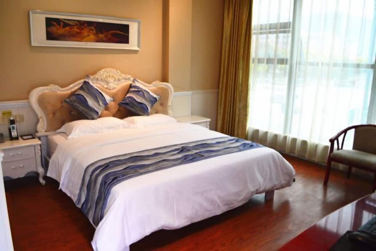 Un lit bien fait, recouvert d’une couvre-lit à rayures, avec un tableau encadré au-dessus, et une chaise placée à droite.