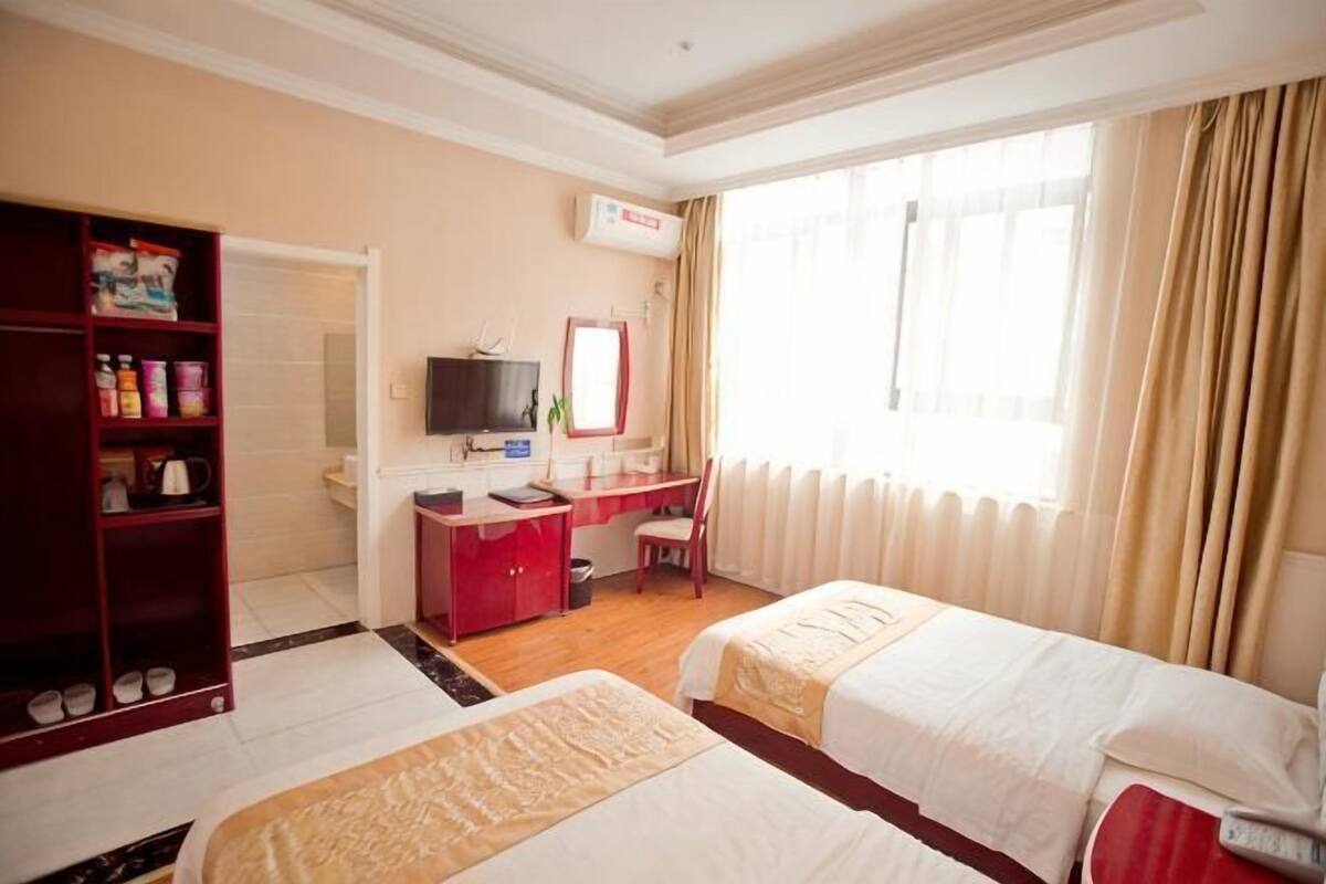 Une chambre d’hôtel avec deux lits, un bureau, une télévision, une armoire et une fenêtre avec des rideaux.