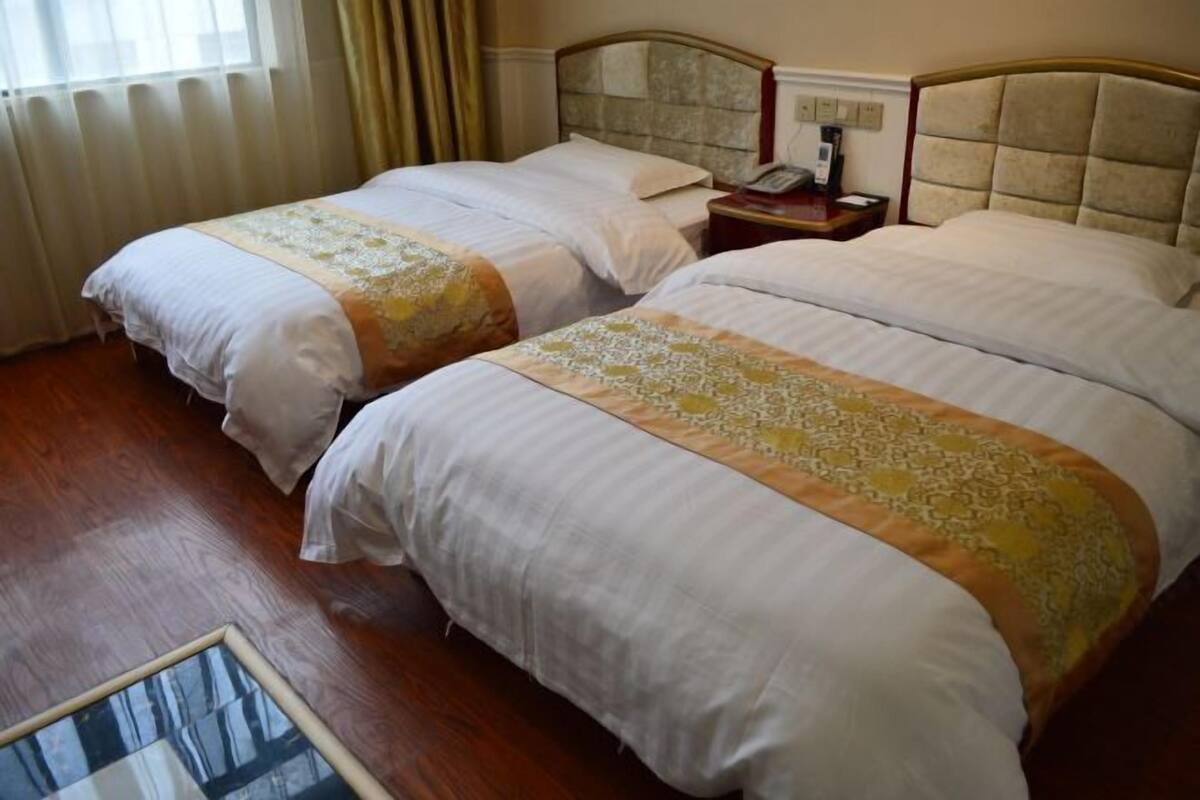Une chambre d’hôtel avec deux lits, un plancher en bois, une table de chevet avec un téléphone et une fenêtre avec des rideaux.