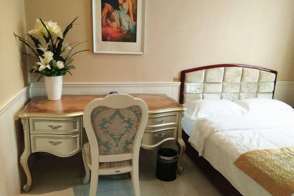 Une chambre à coucher comprenant un lit, une table de chevet, une chaise, un bureau et une poubelle.