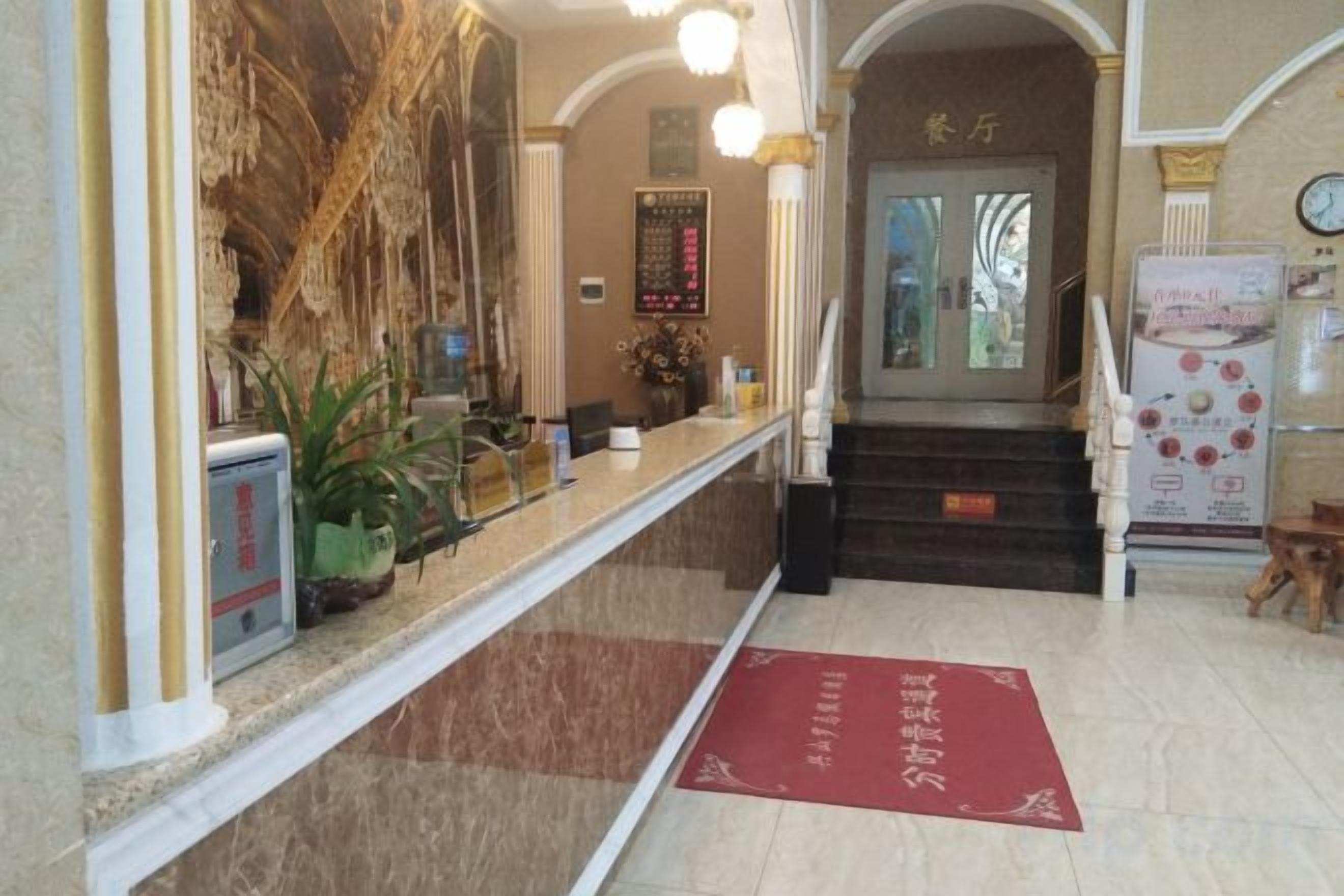A hotel reception area with a marble counter, a red carpet, and a staircase leading to the entrance.