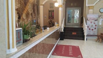 A hotel reception area with a marble counter, a red carpet, and a staircase leading to the entrance.