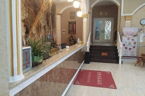 Un hall d’accueil d’hôtel avec un comptoir en marbre, une moquette rouge et un escalier menant à l’entrée.