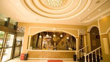 A hotel reception area with a curved counter, a staircase, and a decorative ceiling.