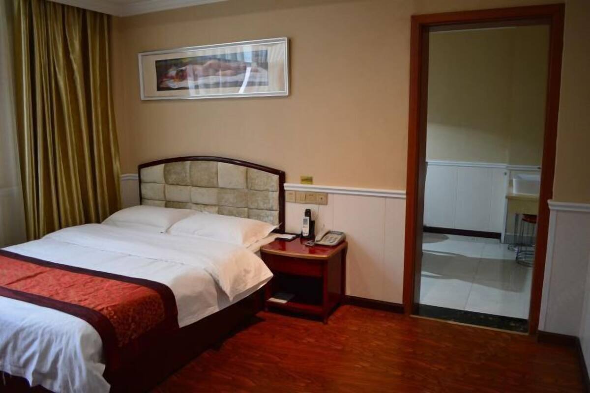 Une chambre d’hôtel comprenant un lit, une table de chevet, un téléphone, un tableau encadré au mur et une porte coulissante donnant accès à la salle de bain.