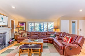 A spacious living room with a large leather sectional sofa, a wooden coffee table, and a fireplace. - BLUE08 - Family-Friendly Sunriver Retreat | Hot Tub + Bikes (Sunriver)